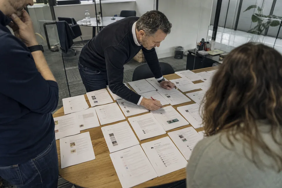 Customer success lead spreading printouts of reviews from several websites across a meeting table to merge duplicates