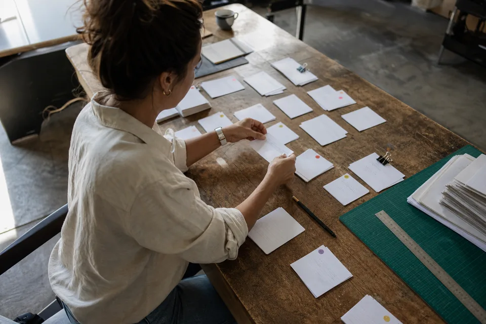 Copywriter sorting printed testimonial drafts into labeled piles on a large worktable, one card in hand