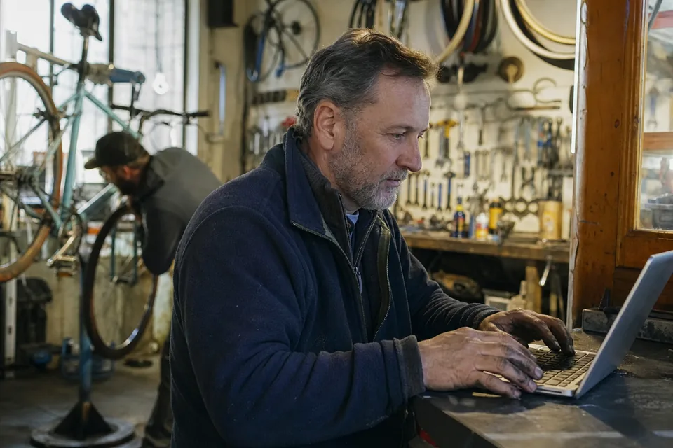 Bike shop owner with a laptop on the workshop counter updating the shop website