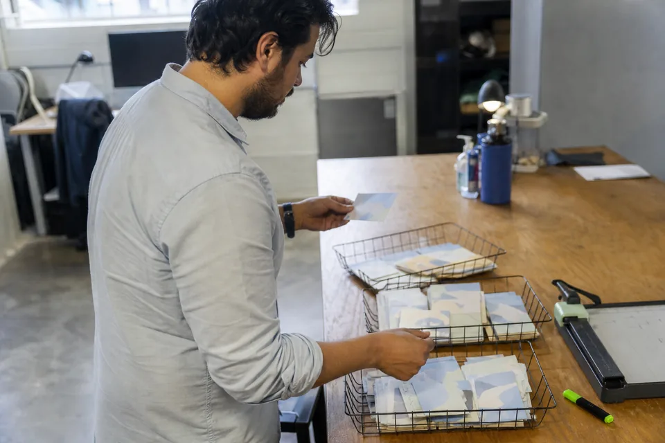 Product marketer sorting printed customer reviews into three labelled trays on a long workbench