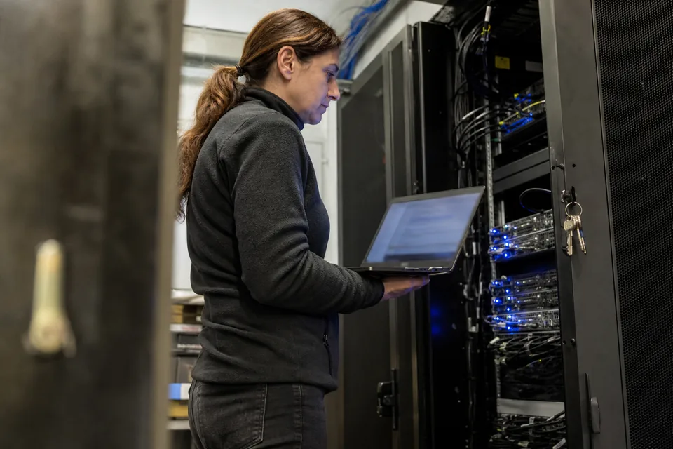 IT administrator checking access settings on a laptop beside a locked server rack