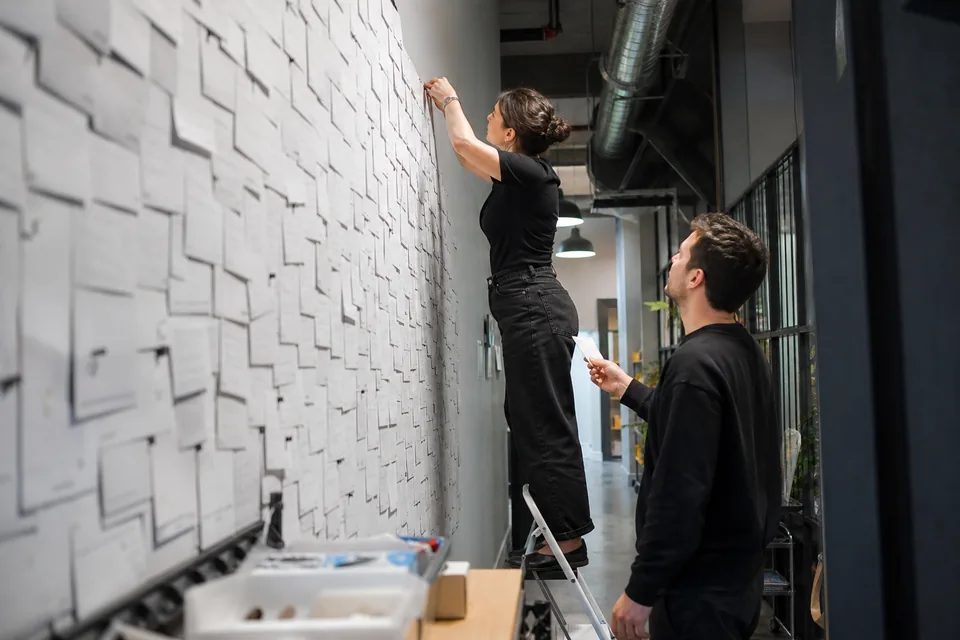 Team pinning dozens of printed customer quotes onto a tall wall in a startup office corridor